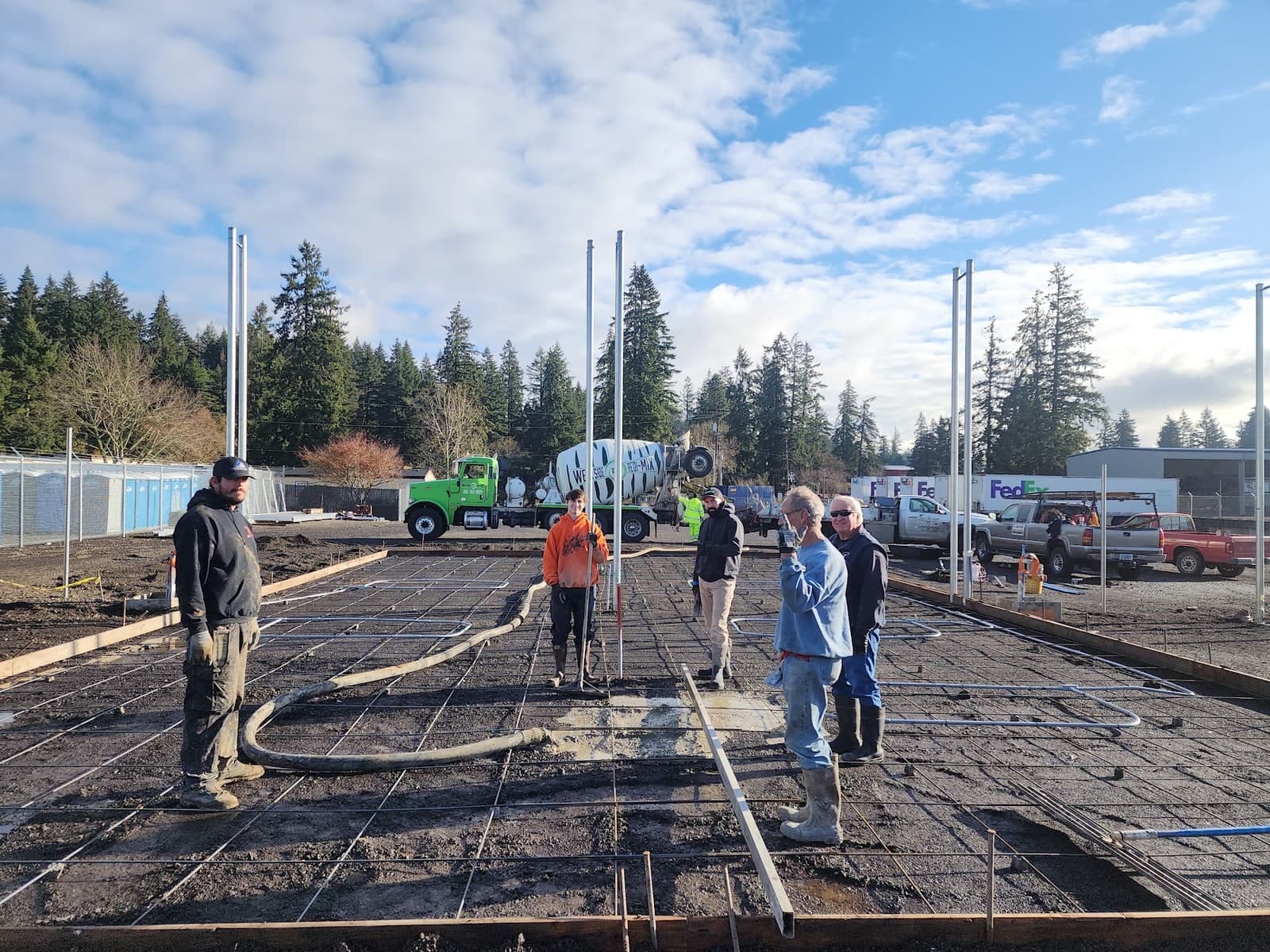 A commercial slab pour under way — a full rebar mat with in-slab piping over compacted base, a placing hose snaked across it and a mixer truck discharging behind the crew
