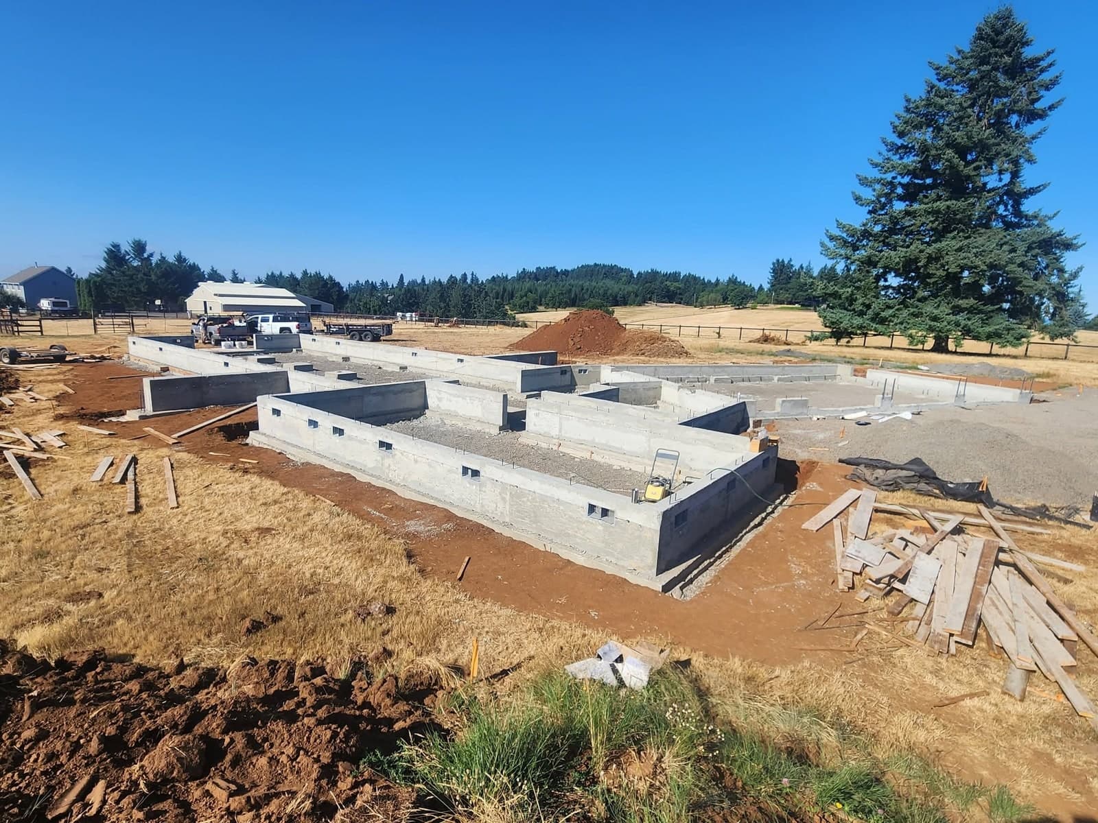 A finished poured foundation for a house — perimeter stem walls, interior bearing walls and crawlspace vents, with stripped form lumber stacked around it